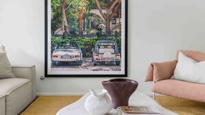 Un salon avec une œuvre d’art encadrée représentant deux voitures, un vase blanc et un magazine posés sur une table basse.