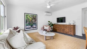 Un salon avec un canapé, une table basse, un téléviseur, un meuble et une grande affiche accrochée au mur.