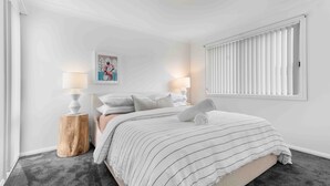 Une chambre à coucher avec un lit, deux lampes de chevet, une fenêtre avec des stores et un tableau encadré au mur.
