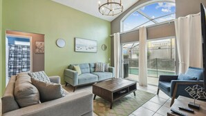 Un salon avec un canapé, une table basse et un meuble pour la télévision. Il y a une fenêtre avec des rideaux et une vue sur l’extérieur.