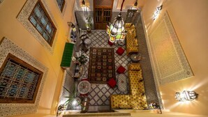 Un intérieur marocain traditionnel, caractérisé par des motifs complexes de carreaux, un tapis central et un espace salon agrémenté de coussins.