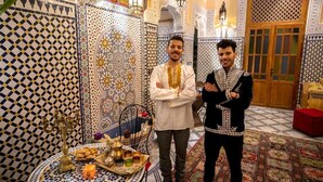 Deux hommes se tiennent debout dans une pièce dont le sol est orné de motifs complexes en mosaïque et qui est décorée dans le style traditionnel marocain.