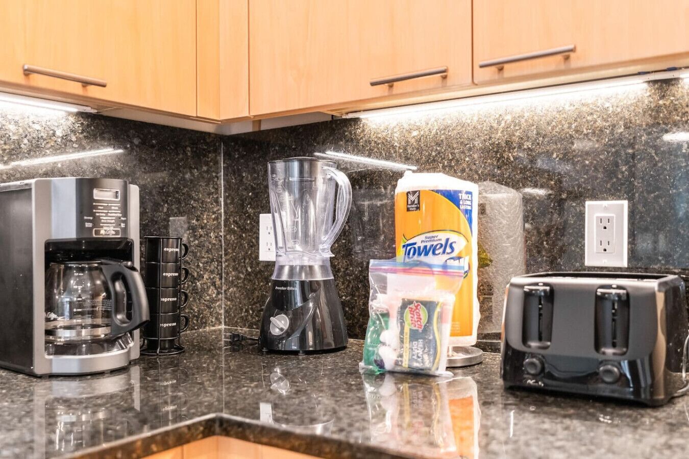 A kitchen with a coffee maker, blender, and toasters on a granite countertop.