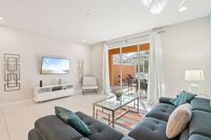 A modern living room with a sofa, TV, and a glass coffee table. - Amazing Family House w pvt Pool - 1605 (Clermont)