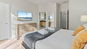 A bedroom with a bed, a TV mounted on the wall, a dresser, and a bathroom visible through an open door. - Amazing Family House w pvt Pool - 1605 (Almont)