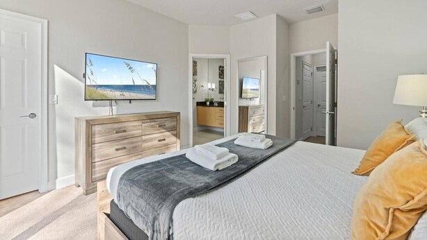 A bedroom with a bed, a TV mounted on the wall, a dresser, and a bathroom visible through an open door. - Amazing Family House w pvt Pool - 1605 (Almont)