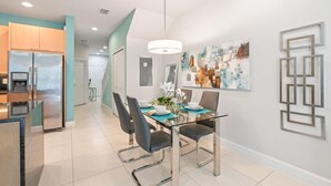 A modern kitchen with a stainless steel refrigerator, a dining area with a glass table and chairs, and a contemporary abstract painting on the wall. - Amazing Family House w pvt Pool - 1605 (Almont)