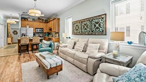 A spacious living room with a beige sofa, a wooden coffee table, and a kitchen in the background. - 🌴Lake + Pool Views | 4 Bikes | Under 550yds to Beach | Paradise 2205 (Santa Rosa Beach)