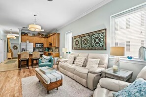 Ein geräumiges Wohnzimmer mit einem beigefarbenen Sofa, einem Holztisch und einer Küche im Hintergrund.