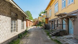 Ein schmaler Gang zwischen Gebäuden mit einem Kiesweg, Holzstufen und einer blauen Tür.