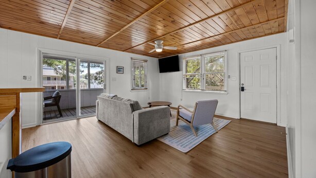 A spacious living room with a wooden ceiling, a grey sofa, a small round table, and a TV mounted on the wall. - Easy Walk to Beach & Nags Head Shops, Restaurants (Nags Head)