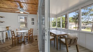 A wooden ceiling, a ceiling fan, a dining table with chairs, a window, and a view of trees and houses. - Easy Walk to Beach & Nags Head Shops, Restaurants (Nags Head)