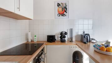 A modern kitchen with white tiles, a black induction cooktop, a coffee maker, and a kettle.