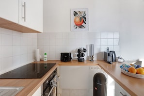Una cocina moderna con baldosas blancas, una placa de inducción negra, una cafetera y un hervidor.