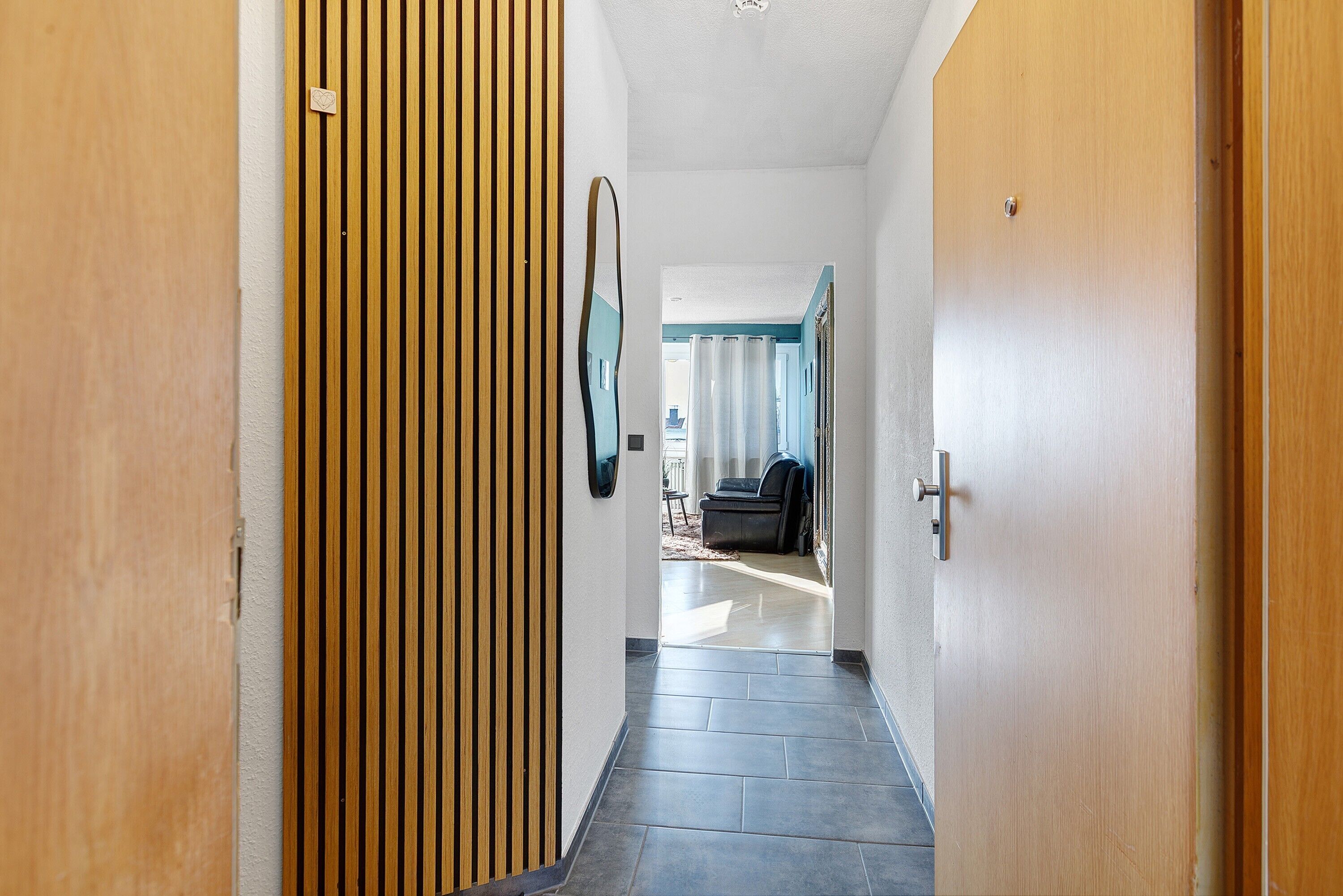 A hallway with a wooden slat wall, a door with a handle, and a tiled floor.