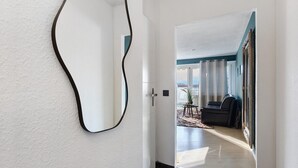 Ein modernes Interieur mit einem gewölbten Spiegel an der Wand, einer Tür, die in einen Wohnbereich mit einer Couch und einem kleinen Tisch führt, und Blick ins Freie.