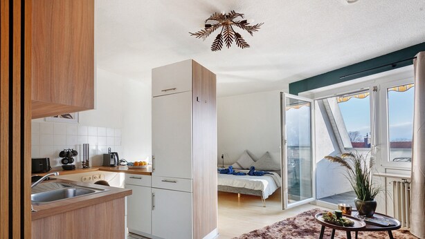 Eine kompakte Wohnung mit Küchenzeile, einem Bett, einer Essecke und Blick auf die Stadt.