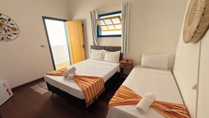 A hotel room with two beds, a window with curtains, a wooden door, and a small bedside table. - Pousada Garden House Tiradentes (Tiradentes)