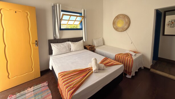 A hotel room with two beds, a window with curtains, a wall decoration, and a door. - Pousada Garden House Tiradentes (Tiradentes)