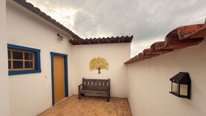 A courtyard with a stone floor, a wooden bench, a wall-mounted lamp, and a decorative tree. - Pousada Garden House Tiradentes (Tiradentes)