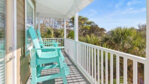 Eine überdachte Veranda mit zwei türkisfarbenen Adirondack-Stühlen, einem weißen Geländer und Blick auf üppige tropische Vegetation.