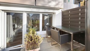 Un espace patio avec une porte vitrée, une table et des chaises, et une plante en pot.