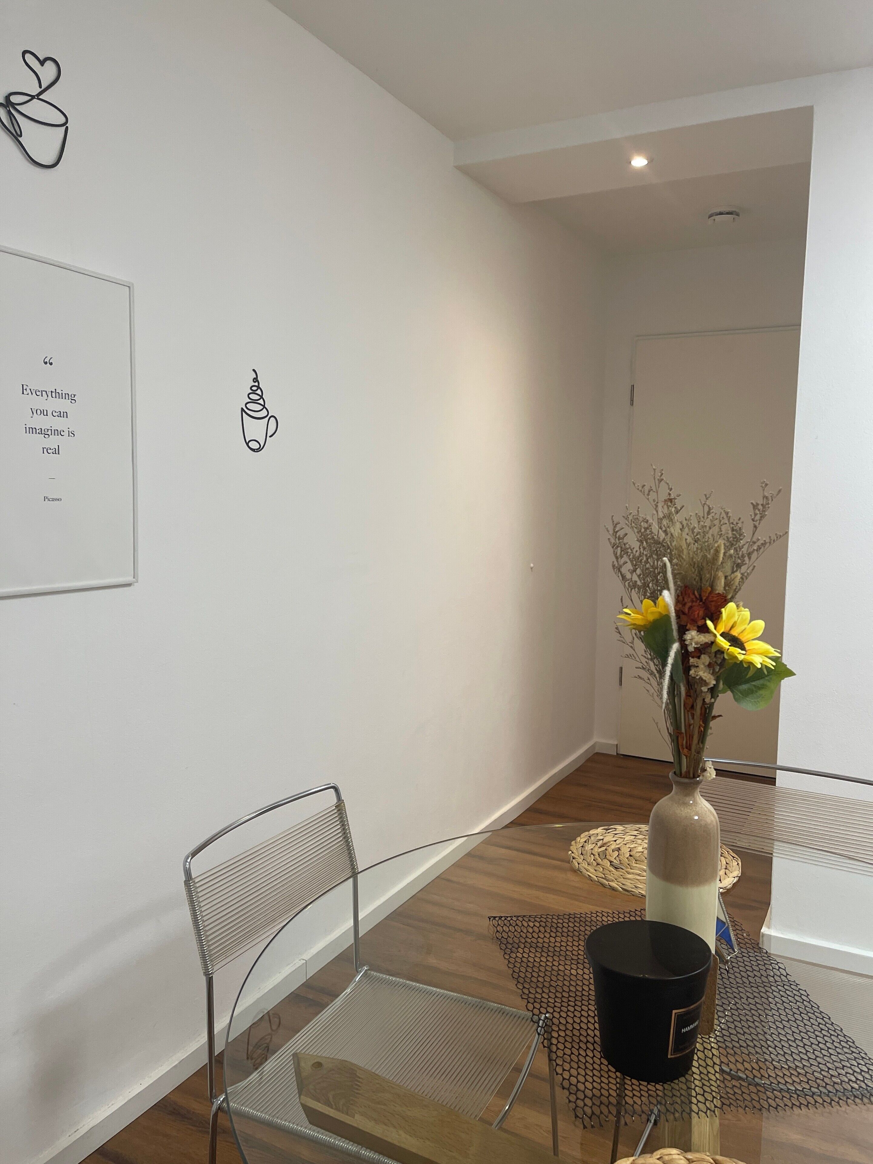 A hallway with a clear glass chair, a vase with flowers, and a black candle on a woven table.
