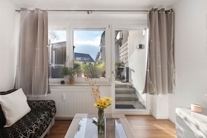 Un soggiorno moderno con un divano, un tavolino da caffè con un vaso di fiori, vista su un balcone attraverso una porta scorrevole e una scala che conduce all'esterno.