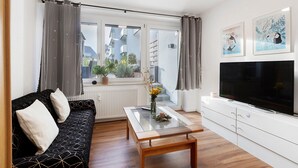 Un salon avec un canapé, une table basse, un téléviseur et une fenêtre avec des rideaux.