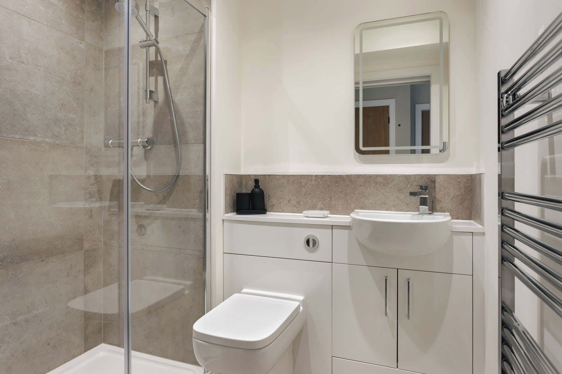 A modern bathroom with a glass-enclosed shower, a white toilet, a sink with a mirror above it, and a towel rack.