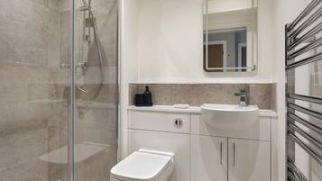 A modern bathroom with a glass-enclosed shower, a white toilet, a sink with a mirror above it, and a towel rack.