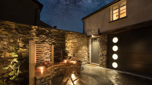 Un bâtiment en pierre avec un banc en bois et une table décorée de bougies, sous un ciel étoilé.