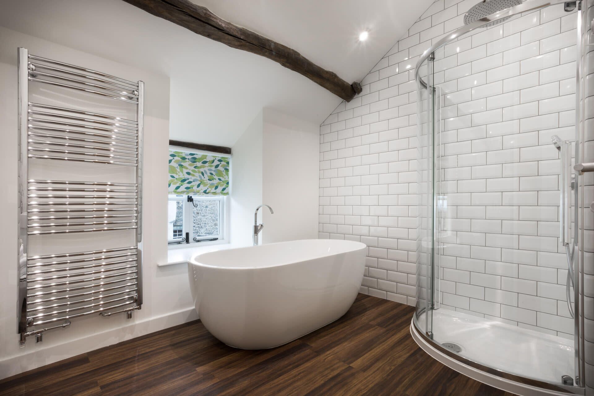 Un baño moderno con una bañera independiente, una ducha con cerramiento de vidrio y un ventanal con persiana de motivos vegetales.