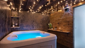 Un bain à remous dans une pièce rustique aux murs en bois, avec une étagère remplie de bouteilles et une plante.
