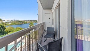A balcony with two wicker chairs, a glass door, and a view of a river and cityscape. - Enclave Studio – 1 mi to Universal w/ Pool (Orlando)