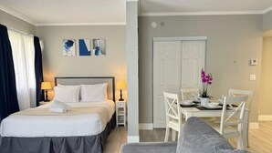A hotel room with a bed, bedside tables, a sofa, a dining table with chairs, and a door leading to another room. - Enclave Studio – 1 mi to Universal w/ Pool (Orlando)