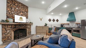 Una sala de estar moderna con chimenea de piedra, un sofá y una zona de comedor con una cocina al fondo.