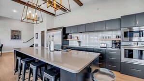 A modern kitchen with a large island, bar stools, stainless steel appliances, and a hanging light fixture. - Lakeview Penthouse Loft w/ Pool, Hot Tub, Game (Osage Beach)