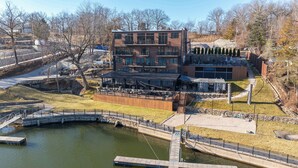 A modern building with multiple floors, outdoor seating, and a small bridge over a water body. - Historic Loft by Pool w/ Lake Access & Hot Tub (Osage Beach)