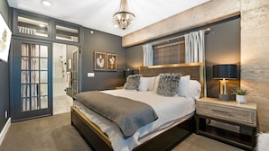 A modern bedroom with a large bed, a nightstand with a lamp, a wall-mounted TV, and a window with curtains. - Historic Loft by Pool w/ Lake Access & Hot Tub (Osage Beach)