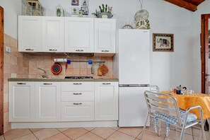 A kitchen with white cabinets, a gas stove, and a dining table with chairs. - Holiday Home 'Trilo Marina' with Private Terrace, Garden and Air Conditioning (San Teodoro)