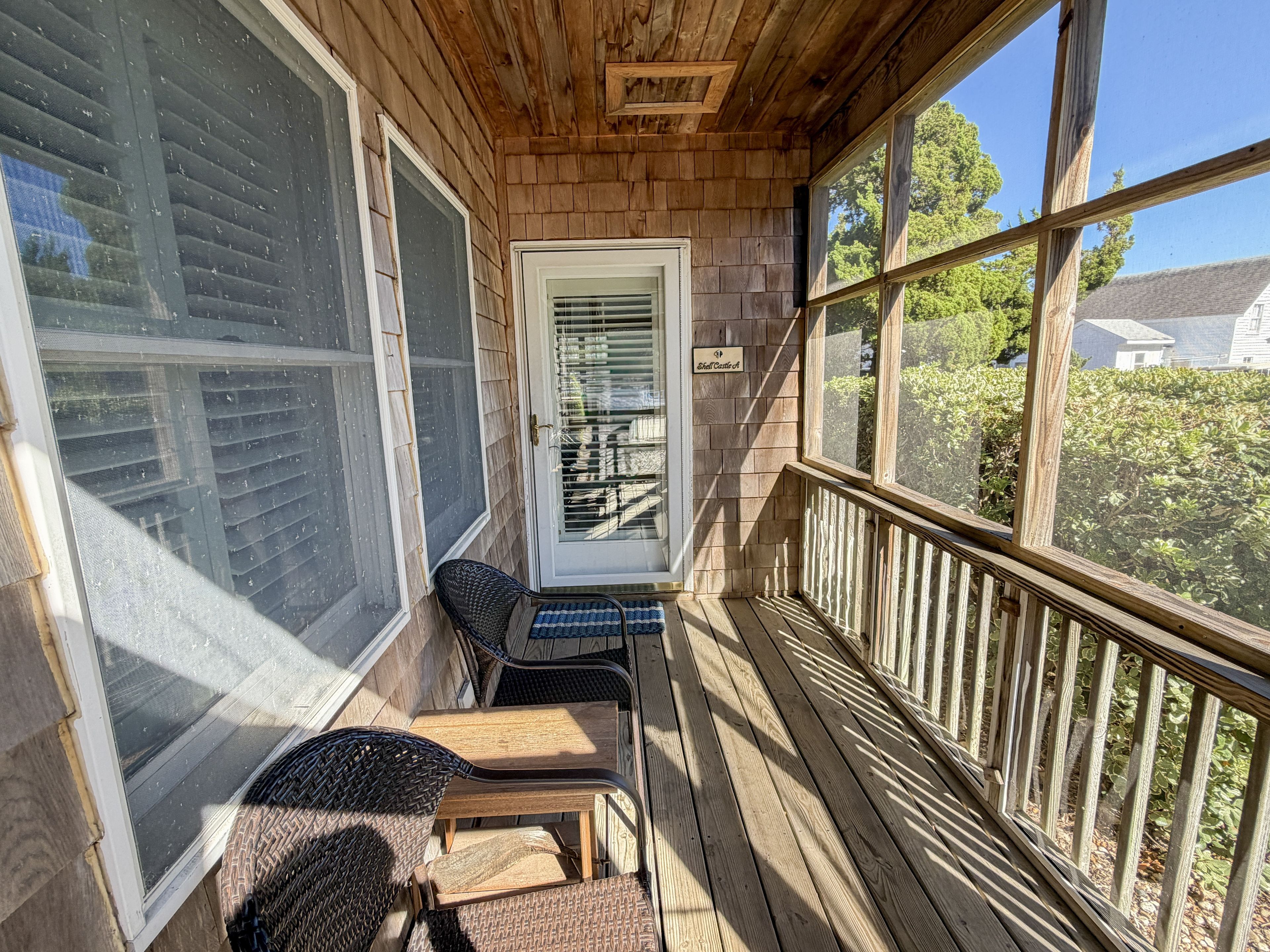 A wooden porch with a door, a small table, and two chairs.