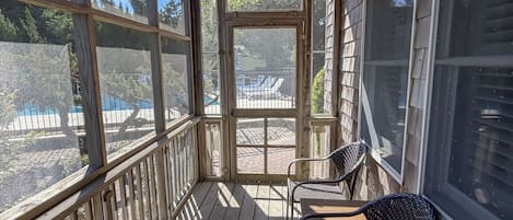 Une terrasse en bois avec un porche couvert, deux fauteuils en osier et une vue sur une piscine et une cour clôturée.
