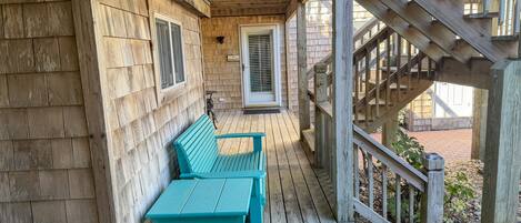 A wooden deck with a bench and table, a covered area with a door, and a wooden staircase.