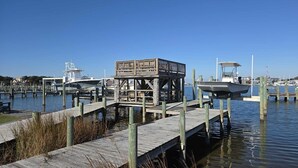 A wooden dock with a wooden structure in the middle, boats docked at the pier, and a clear blue sky in the background. - CV8B: Studio with Balcony (Ocracoke)