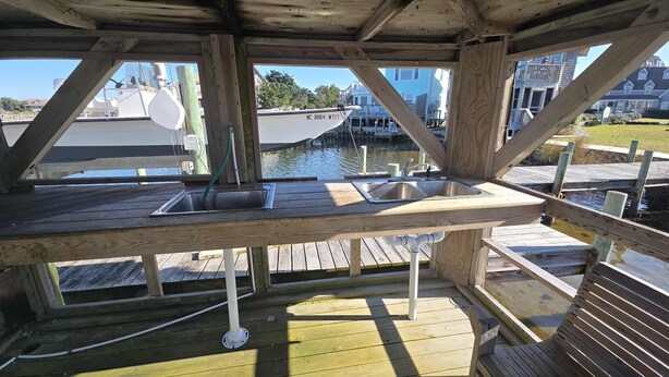 A wooden deck with a built-in sink and a view of a dock with a boat.