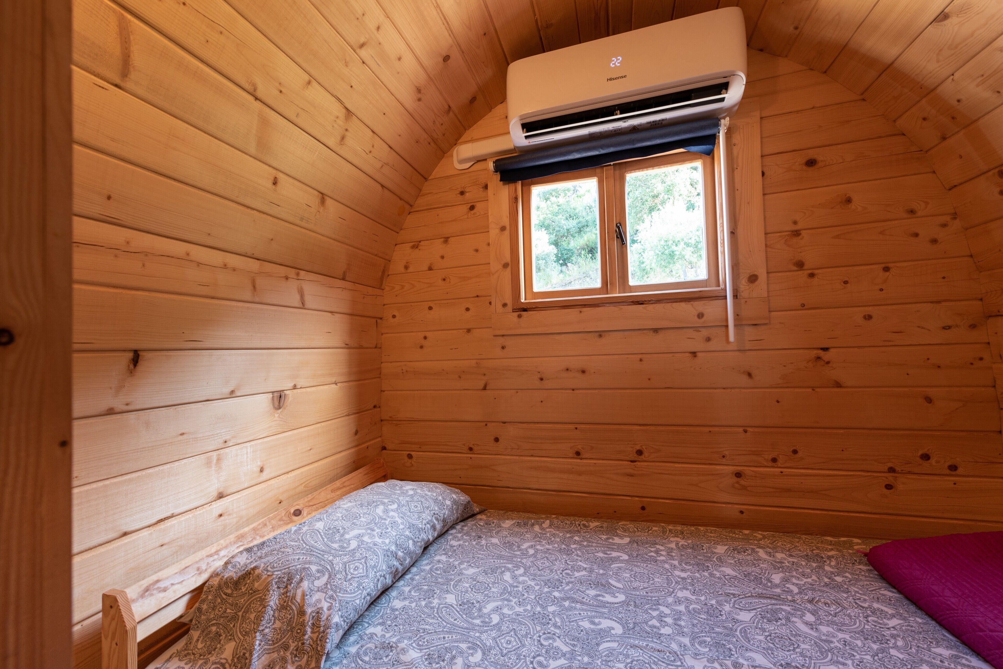A wooden cabin room with a bed, a window, and an air conditioning unit.