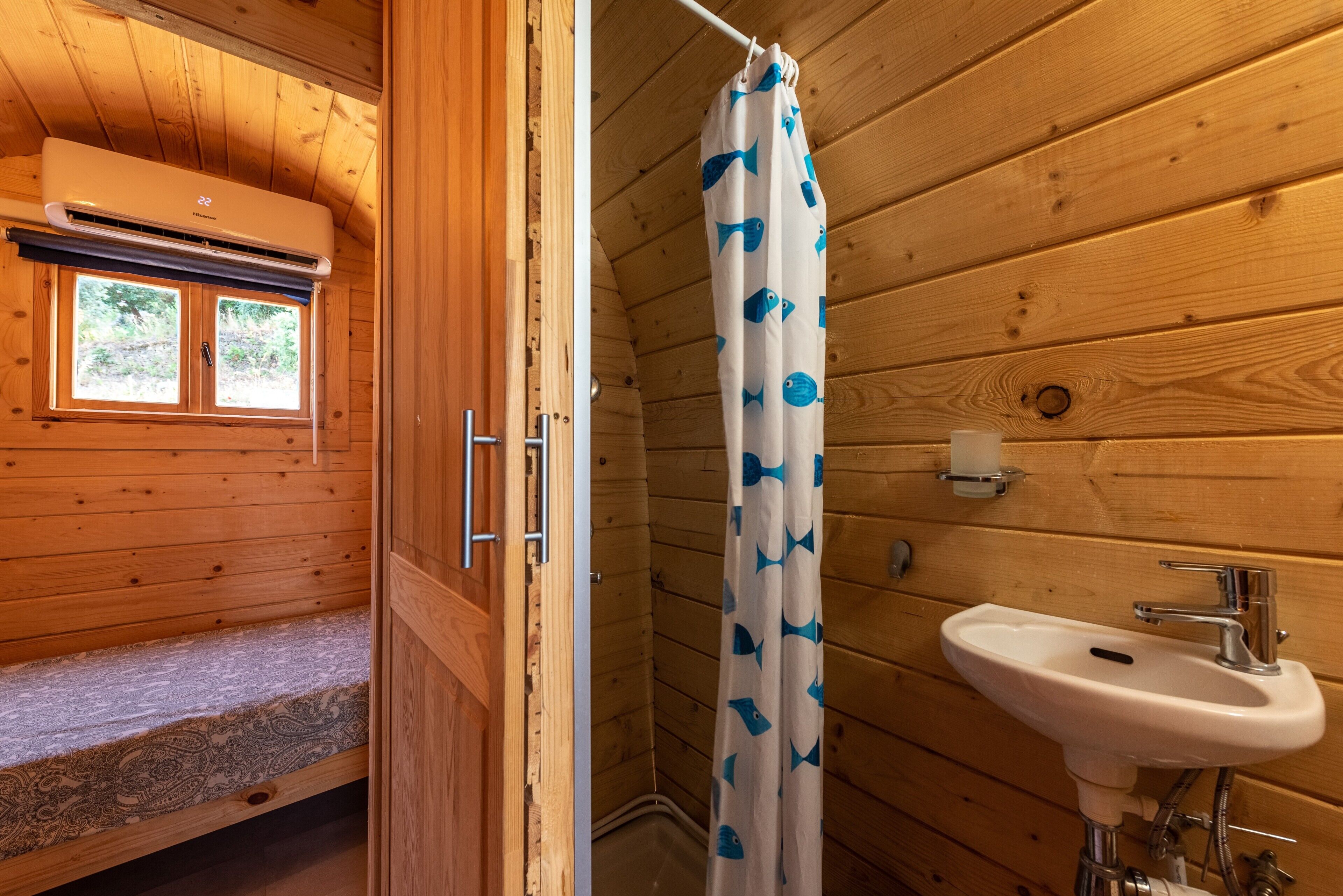 Ein Badezimmer einer Holzhütte mit Fenster, Duschvorhang, Waschbecken und einer Bank.