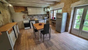 Eine rustikale Küche mit Holzdielen, weißen Schränken, einem Esstisch mit Stühlen und einem Kühlschrank.