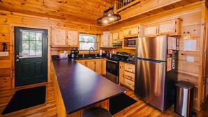 A wooden cabin interior with a kitchen featuring a long counter, stainless steel appliances, and a black door. - New River Log Cabin | Waterfront • Sauna • Jet Tub (Pulaski County)